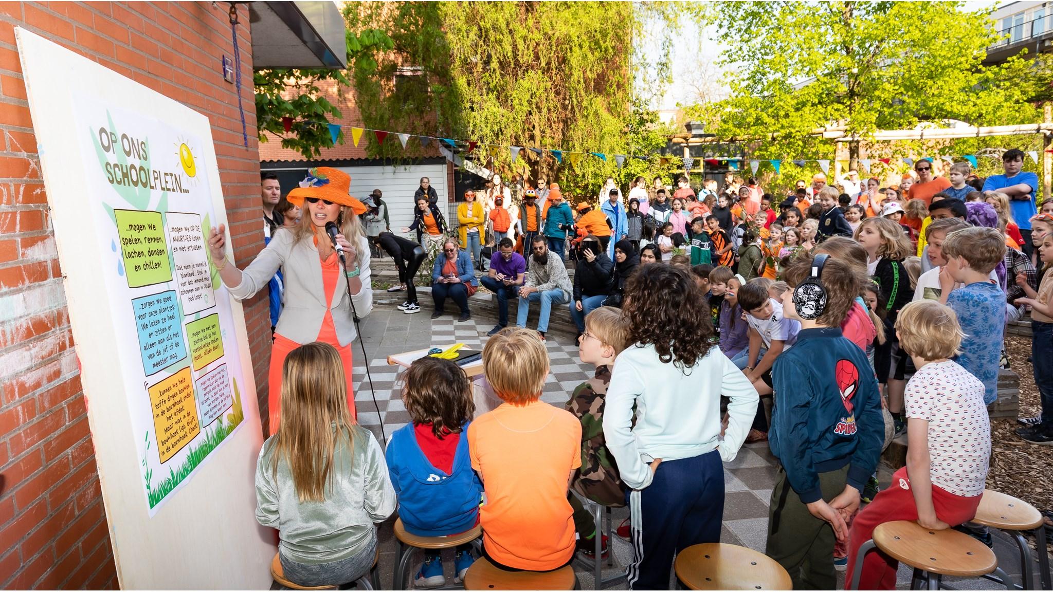 Een kleurrijke bijeenkomst op het schoolplein van Quadratum in Rotterdam, waar kinderen enthousiast luisteren naar een presentatie.