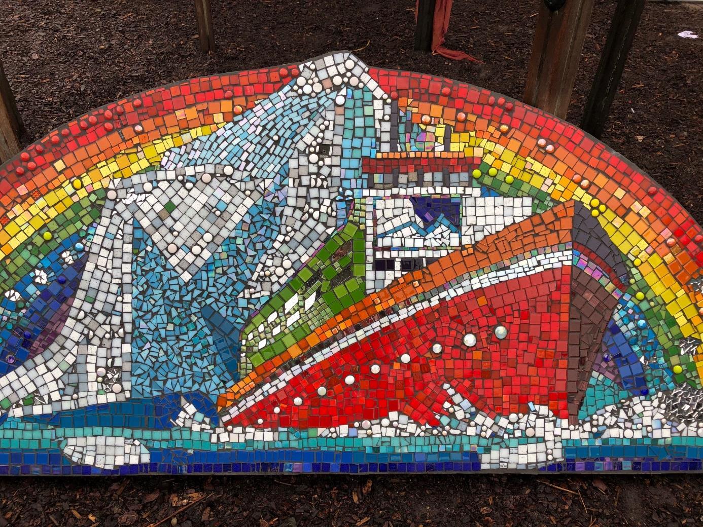 Een kleurrijke mozaïek van een schip met bergen en een regenboog op het schoolplein van Dalton Kind Centrum De IJsbreker in Amsterdam.