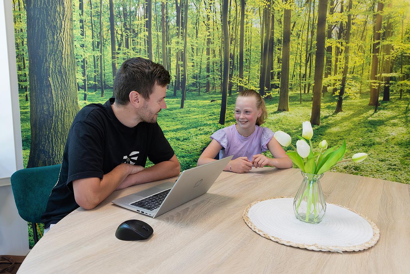 Een lachende leerling en een leraar observeren een laptop in de klas van obs De Dennenkamp in Ommen. Een lachende leerling en een leraar observeren een laptop in de klas van obs De Dennenkamp in Ommen.