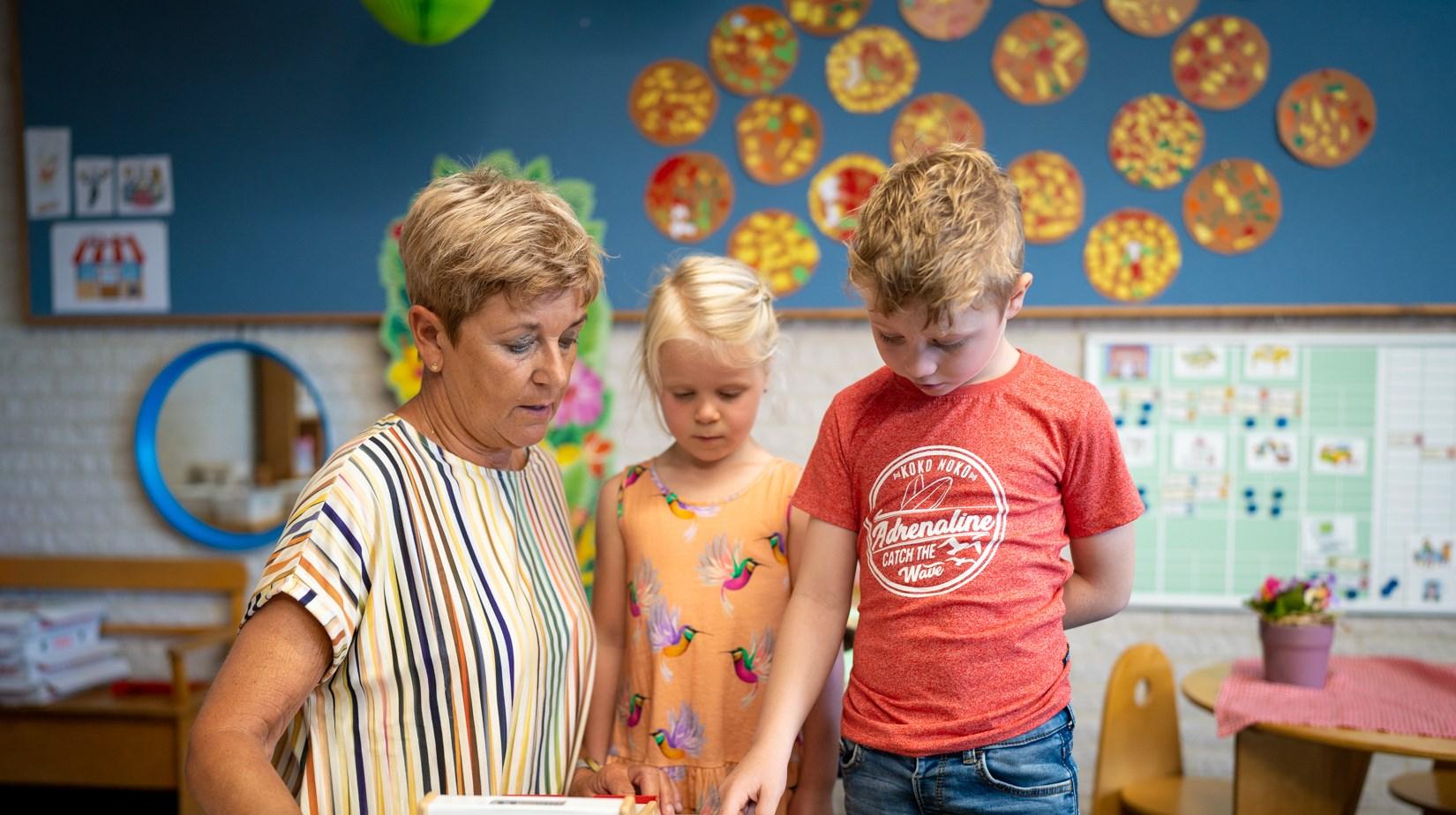 Een leerkracht van Basisschool De Hovenier in Montfort helpt twee kinderen bij hun activiteit in de klas. Een leerkracht van Basisschool De Hovenier in Montfort helpt twee kinderen bij hun activiteit in de klas.