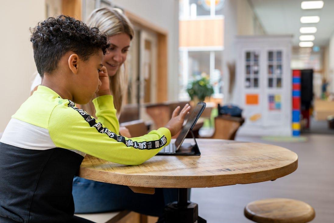 Een leerling en een lerares van Synergieschool St Alfonsus voor basisonderwijs in Roermond werken samen op een tablet aan een ronde houten tafel. Een leerling en een lerares van Synergieschool St Alfonsus voor basisonderwijs in Roermond werken samen op een tablet aan een ronde houten tafel.