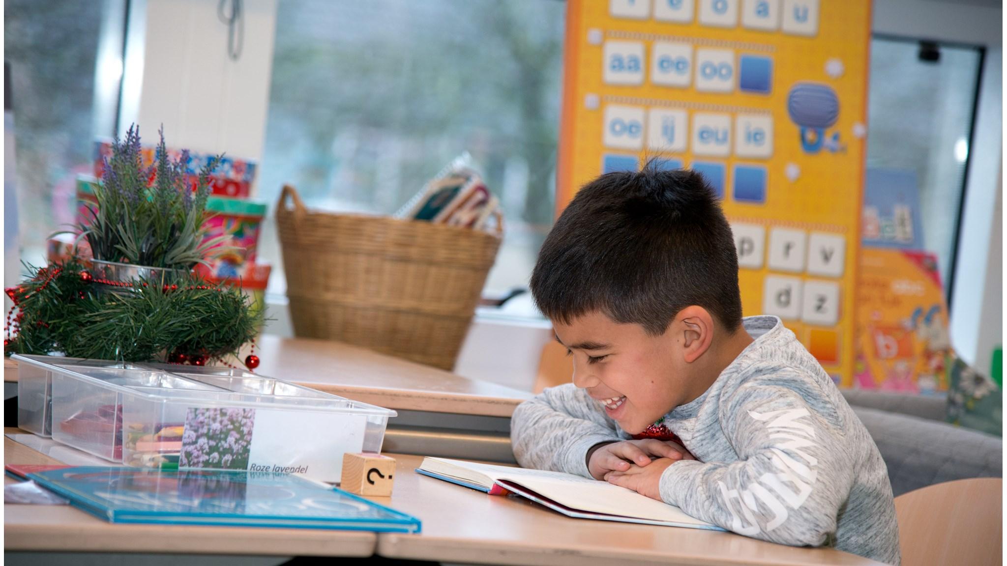 Een leerling lacht terwijl hij in zijn boek leest in de Kruidenhoek Jenaplan Basisschool in Rotterdam. Een leerling lacht terwijl hij in zijn boek leest in de Kruidenhoek Jenaplan Basisschool in Rotterdam.