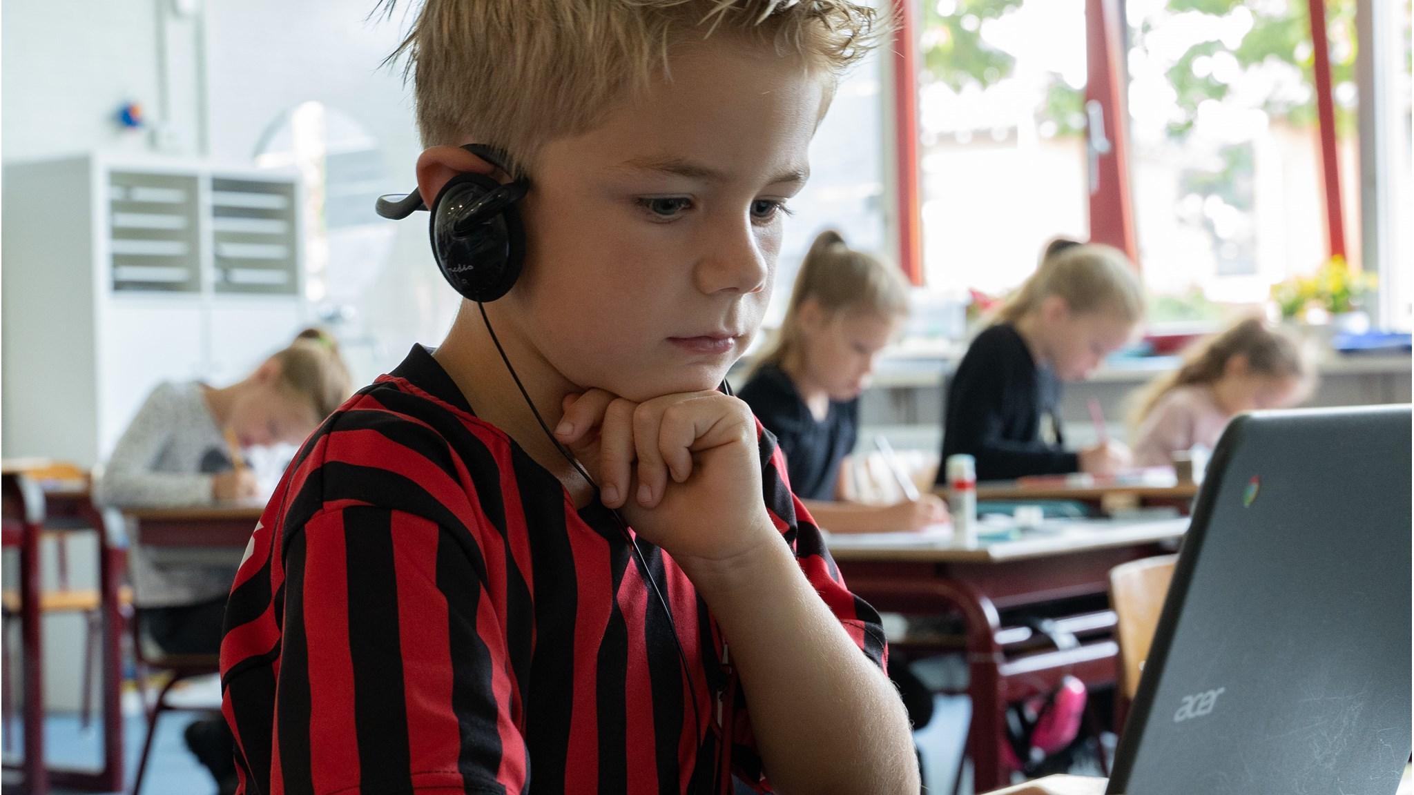 Een leerling met een koptelefoon werkt geconcentreerd aan een laptop in de klas van Willibrord in Denekamp. Een leerling met een koptelefoon werkt geconcentreerd aan een laptop in de klas van Willibrord in Denekamp.