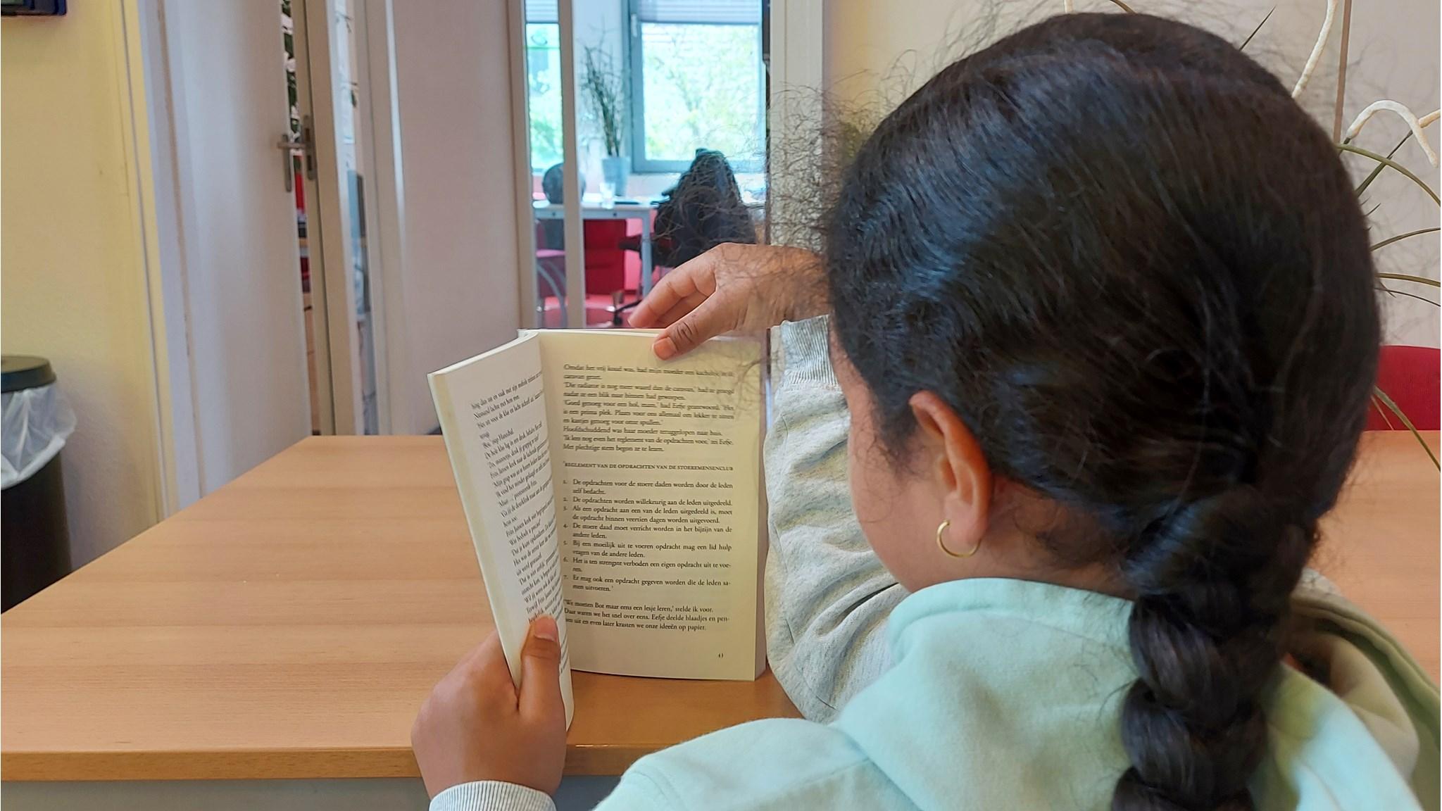 Een leerling van basisschool Onze Wereld in Amsterdam leest een boek aan een houten tafel. Een leerling van basisschool Onze Wereld in Amsterdam leest een boek aan een houten tafel.