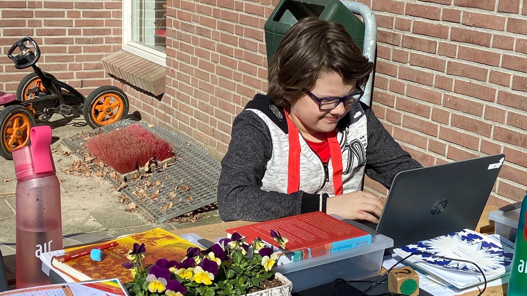 Een leerling van Basisschool Stokkum in Markelo voert zijn schoolwerk uit aan een bureau buiten op het schoolplein. Een leerling van Basisschool Stokkum in Markelo voert zijn schoolwerk uit aan een bureau buiten op het schoolplein.