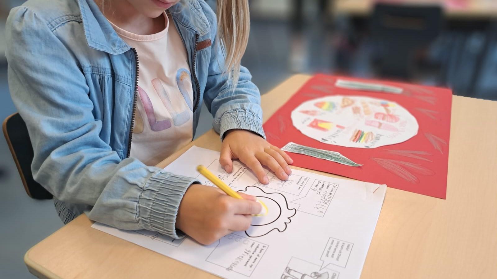 Een leerling van de Oranje Nassauschool in Geldermalsen is bezig met tekenen en schrijven op een schooltafel. Een leerling van de Oranje Nassauschool in Geldermalsen is bezig met tekenen en schrijven op een schooltafel.