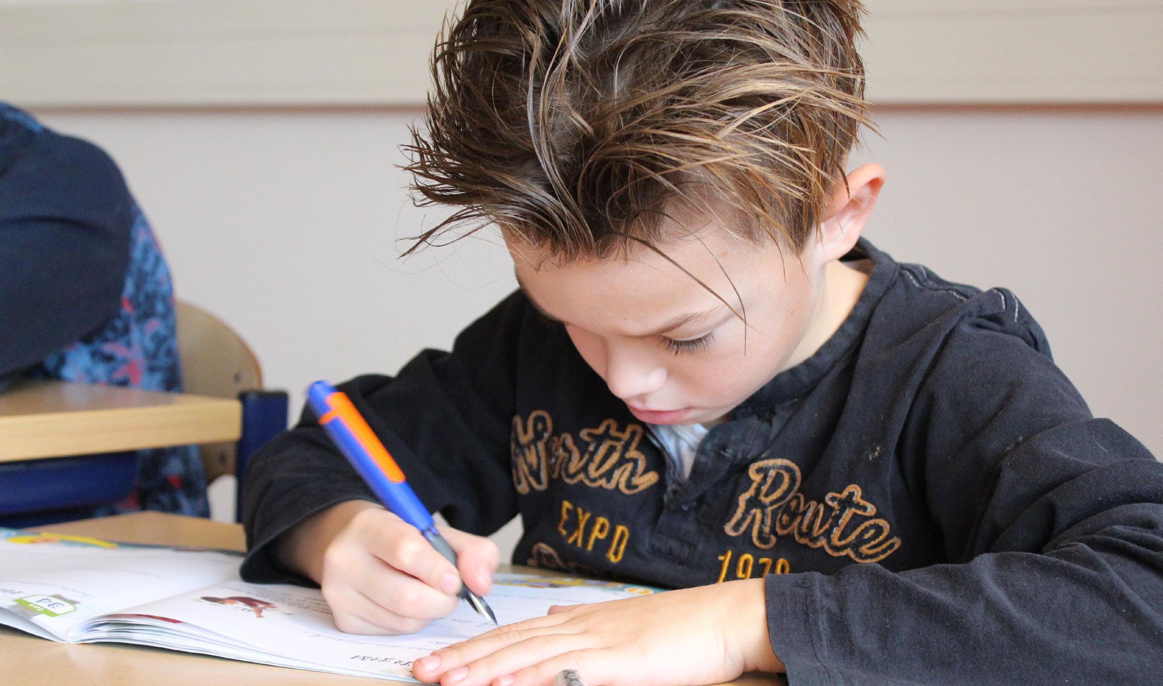 Een leerling van de Paasbergschool in Ede is geconcentreerd aan het schrijven in de klas.