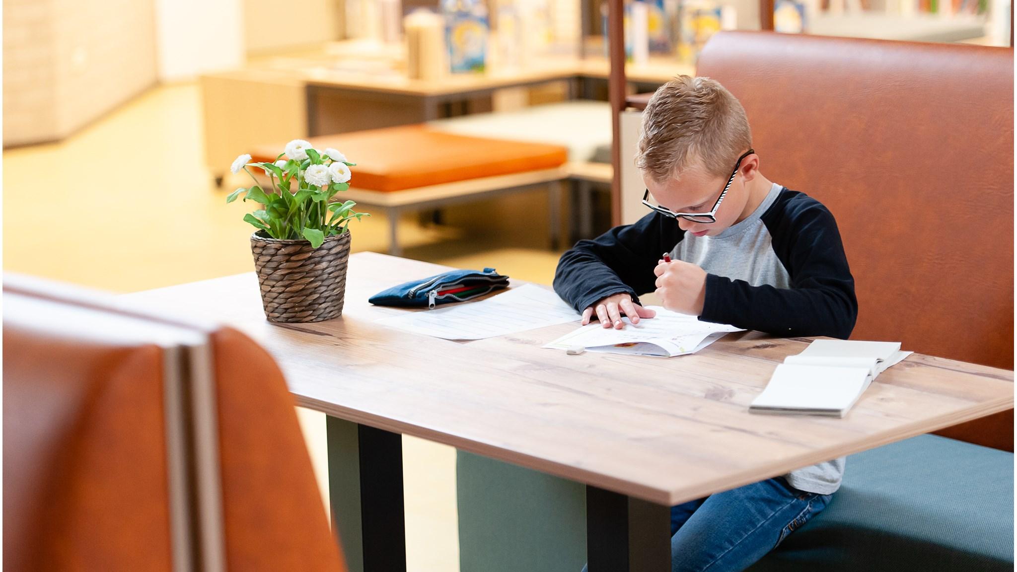 Een leerling van Integraal Kind Centrum Het Klokhuis in Duiven maakt huiswerk aan een houten tafel. Een leerling van Integraal Kind Centrum Het Klokhuis in Duiven maakt huiswerk aan een houten tafel.