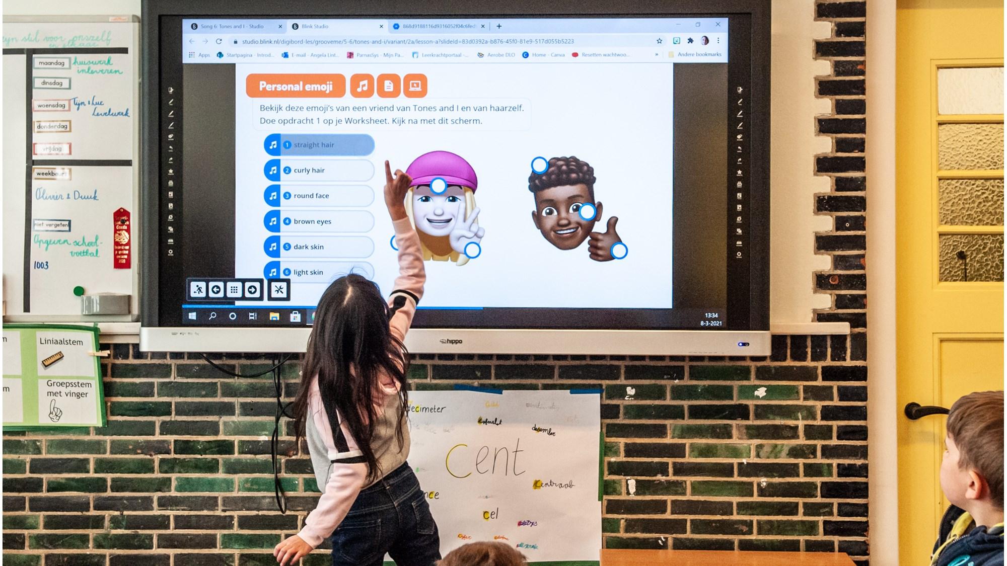 Een leerling van Kindcentrum De Heijberg in Rotterdam wijst naar emoji's op het scherm tijdens een interactieve les.
