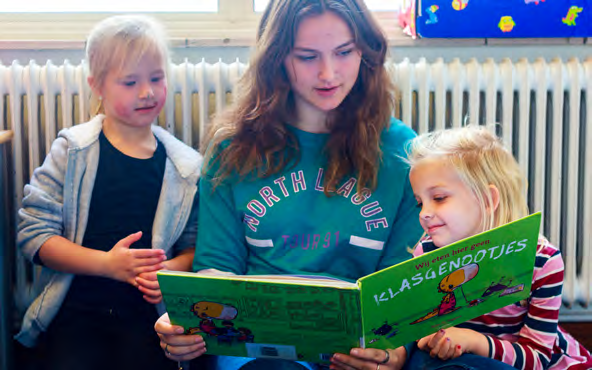 Een leerling van School Paulus in Enschede leest samen met twee kinderen een boek. Een leerling van School Paulus in Enschede leest samen met twee kinderen een boek.