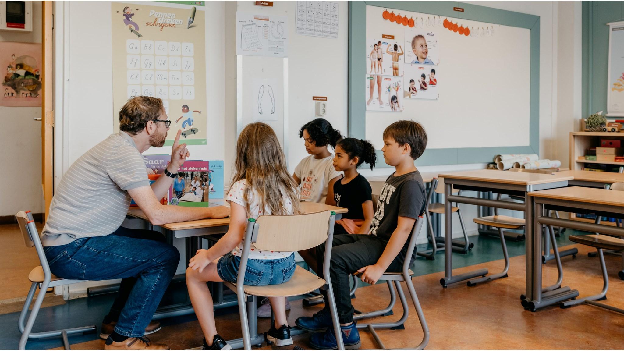 Een leraar geeft uitleg aan een groep leerlingen in de klas van de Goede Herderschool in Rotterdam. Een leraar geeft uitleg aan een groep leerlingen in de klas van de Goede Herderschool in Rotterdam.