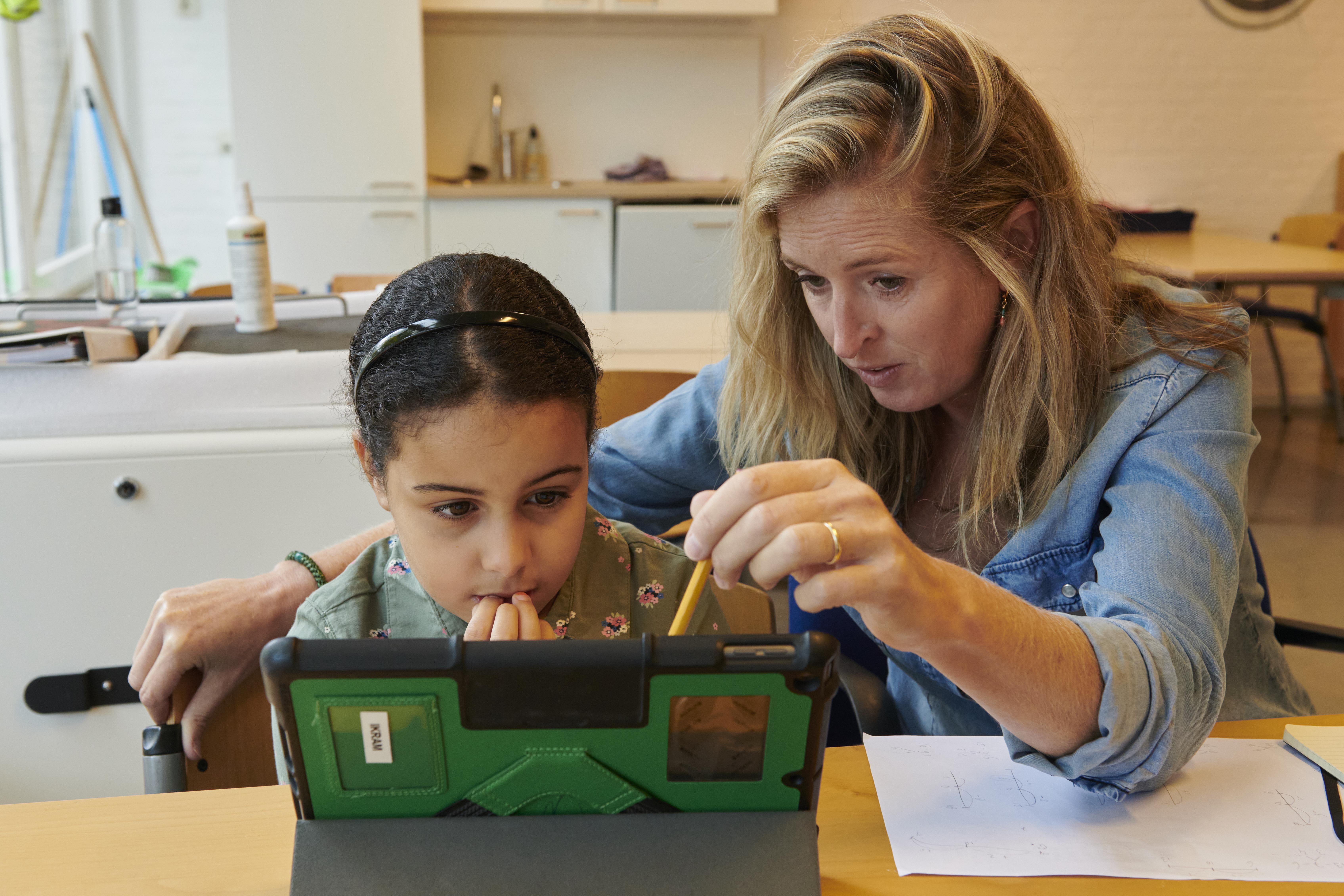 Een lerares helpt een meisje met een tablet in OBS de Globe in Haarlem. Een lerares helpt een meisje met een tablet in OBS de Globe in Haarlem.
