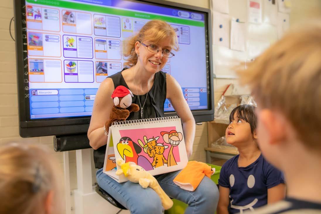 Een lerares van PCBO De Wonderboom in Amersfoort presenteert een interactieve les aan kinderen met behulp van een kleurboek en een handpop.
