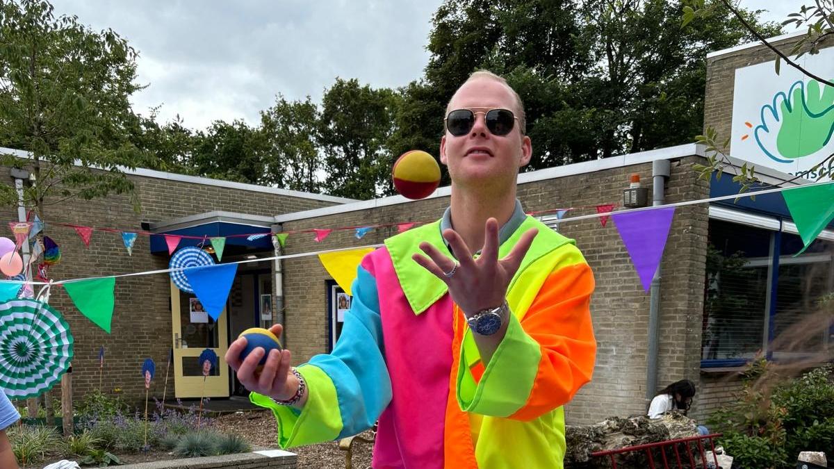 Een man in een kleurrijk kostuum jongleert met ballen op het schoolplein van de Sjaloomschool in Katwijk (Zuid-Holland). Een man in een kleurrijk kostuum jongleert met ballen op het schoolplein van de Sjaloomschool in Katwijk (Zuid-Holland).