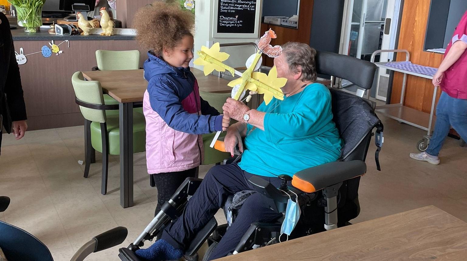 Een meisje geeft een creatief bloemstuk aan een oudere vrouw in Communityschool De Kameleon in Zwanenburg.