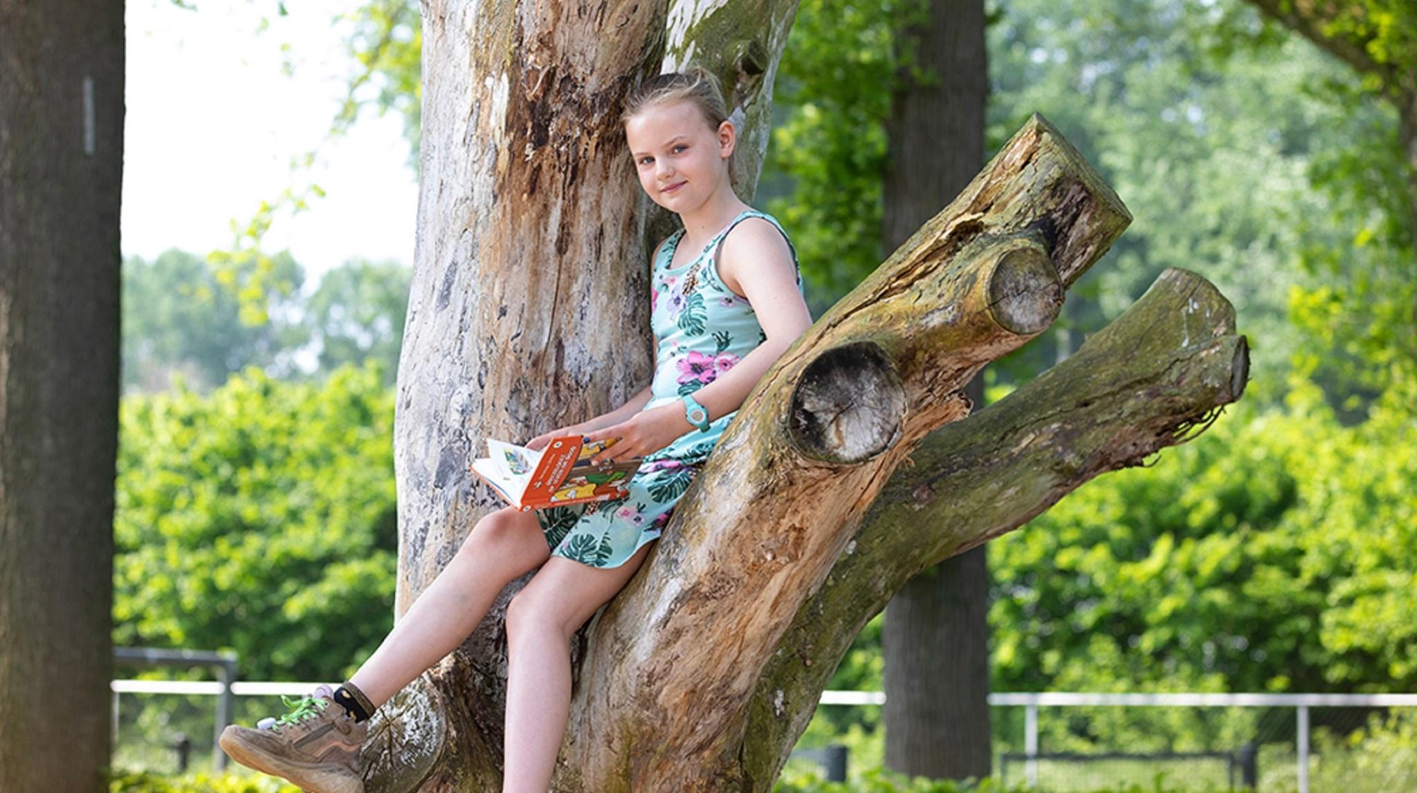 Een meisje leest een boek terwijl ze op een boomzitplaats zit op het schoolplein van Montessori Sterrenschool Geerstraat in Vaassen. Een meisje leest een boek terwijl ze op een boomzitplaats zit op het schoolplein van Montessori Sterrenschool Geerstraat in Vaassen.