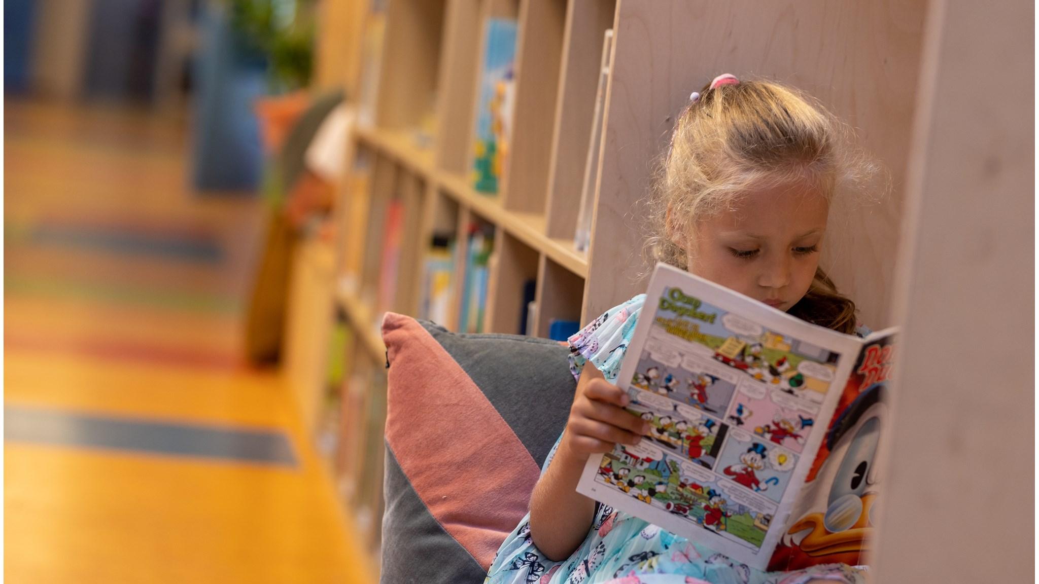 Een meisje leest een stripboek terwijl ze ontspannen zit in de leeshoek van Basisschool De Cirkel in Gouda. Een meisje leest een stripboek terwijl ze ontspannen zit in de leeshoek van Basisschool De Cirkel in Gouda.