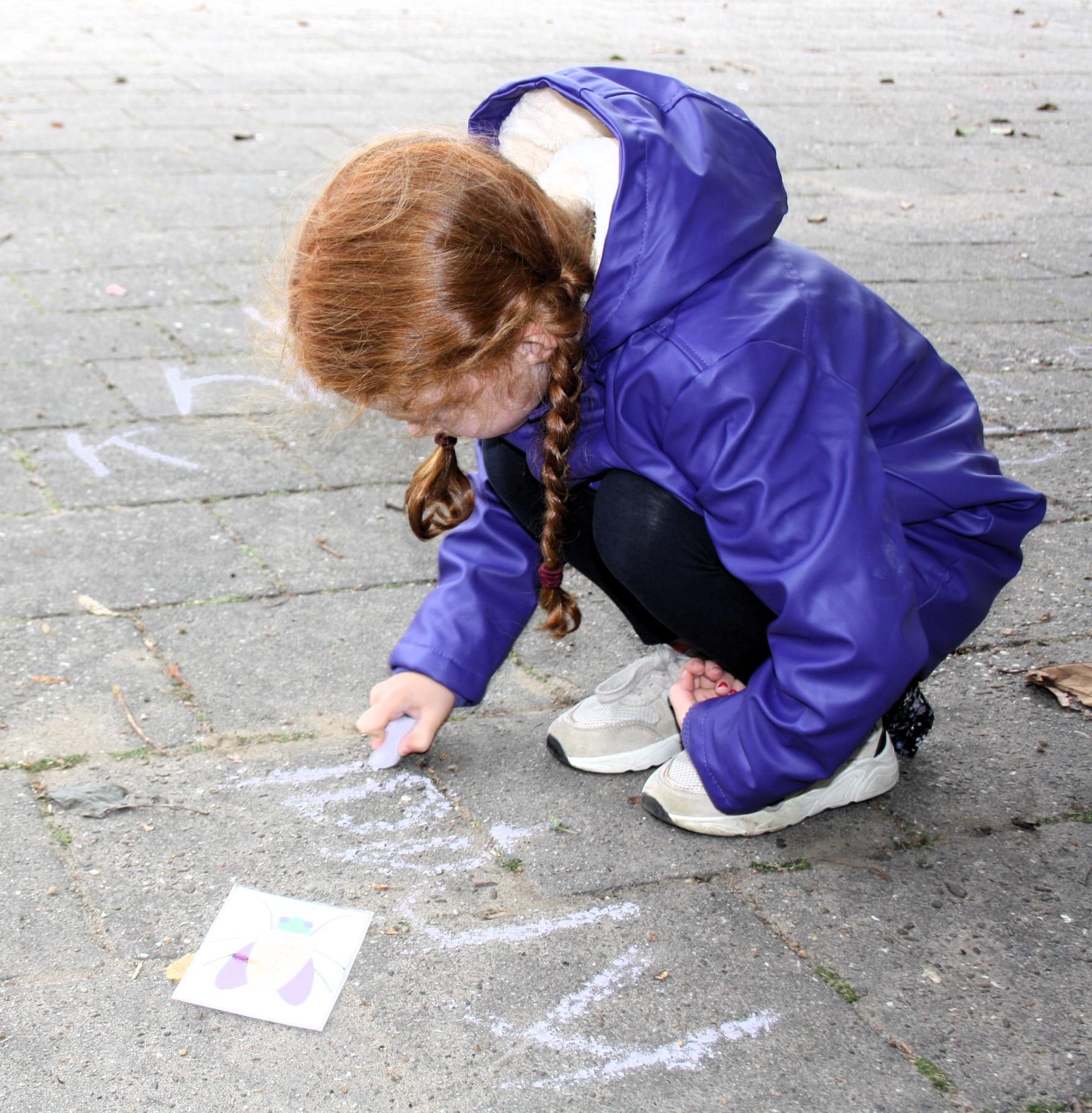 Een meisje met een paarse jas tekent met krijt op het schoolplein van Basisschool Jan Ligthart in Zelhem.