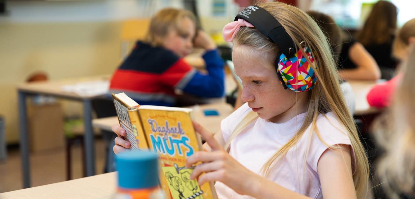 Een meisje met kleurrijke hoofdtelefoon leest een boek in de klas van de Jozefschool Katholiek Basisonderwijs in Aalsmeer. Een meisje met kleurrijke hoofdtelefoon leest een boek in de klas van de Jozefschool Katholiek Basisonderwijs in Aalsmeer.