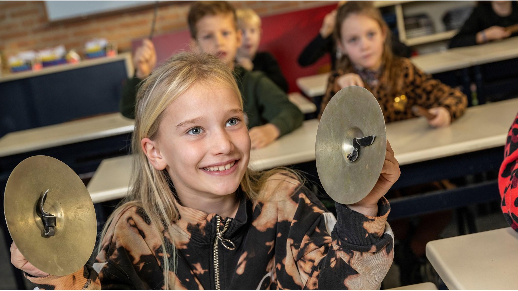Een meisje speelt met cymbalen in de klas van Basisschool De Horizon in Grashoek. Een meisje speelt met cymbalen in de klas van Basisschool De Horizon in Grashoek.