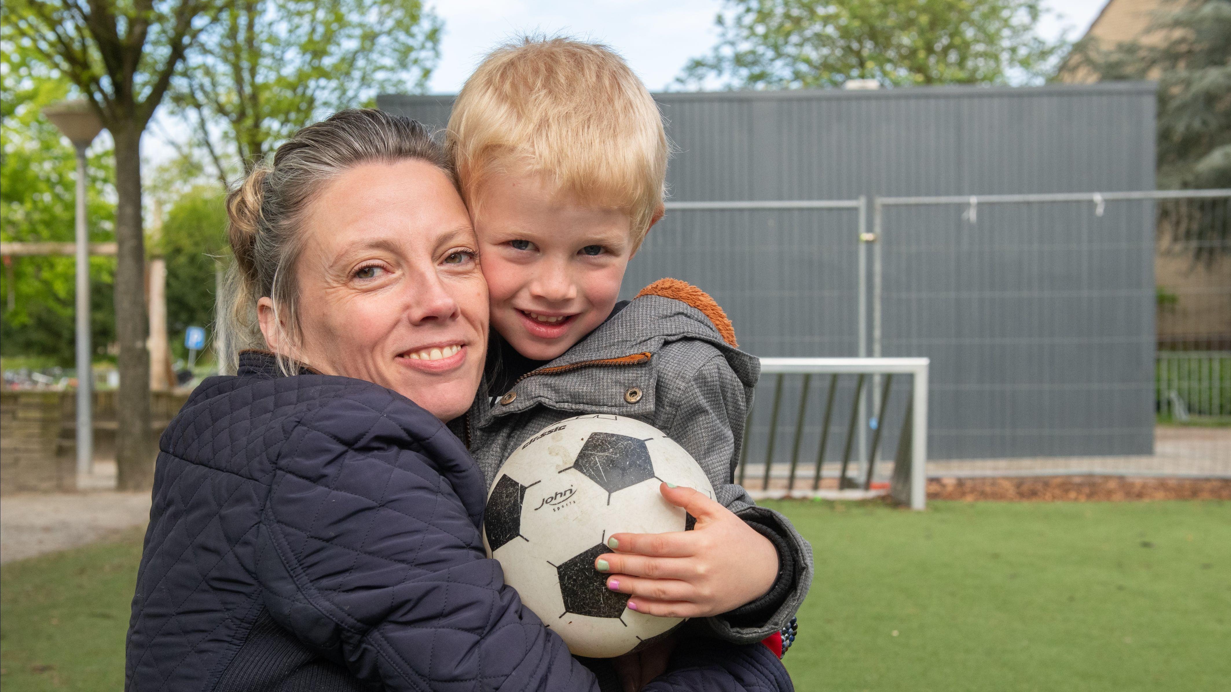 Een moeder en haar zoon poseren gelukkig op het schoolplein van De Vliegeniers in Barneveld, terwijl hij een voetbal vasthoudt. Een moeder en haar zoon poseren gelukkig op het schoolplein van De Vliegeniers in Barneveld, terwijl hij een voetbal vasthoudt.
