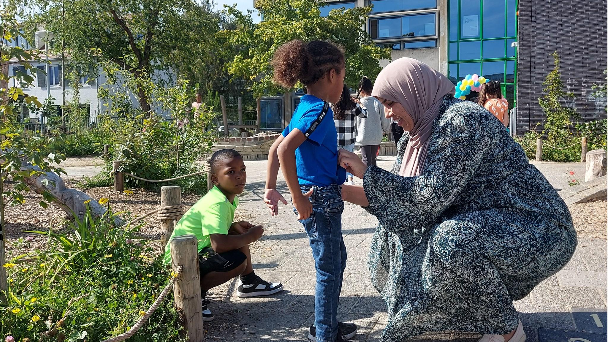 Een moeder helpt haar kind met zijn kleding op het schoolplein van Onze Wereld in Amsterdam. Een moeder helpt haar kind met zijn kleding op het schoolplein van Onze Wereld in Amsterdam.