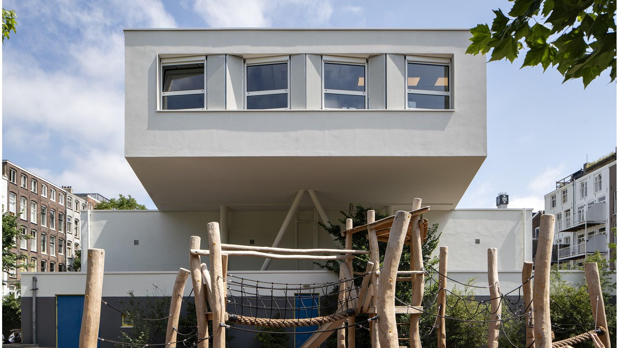 Foto van de Dr. E. Boekmanschool in Amsterdam met een modern schoolgebouw en een houten speeltoestel op het schoolplein. Foto van de Dr. E. Boekmanschool in Amsterdam met een modern schoolgebouw en een houten speeltoestel op het schoolplein.