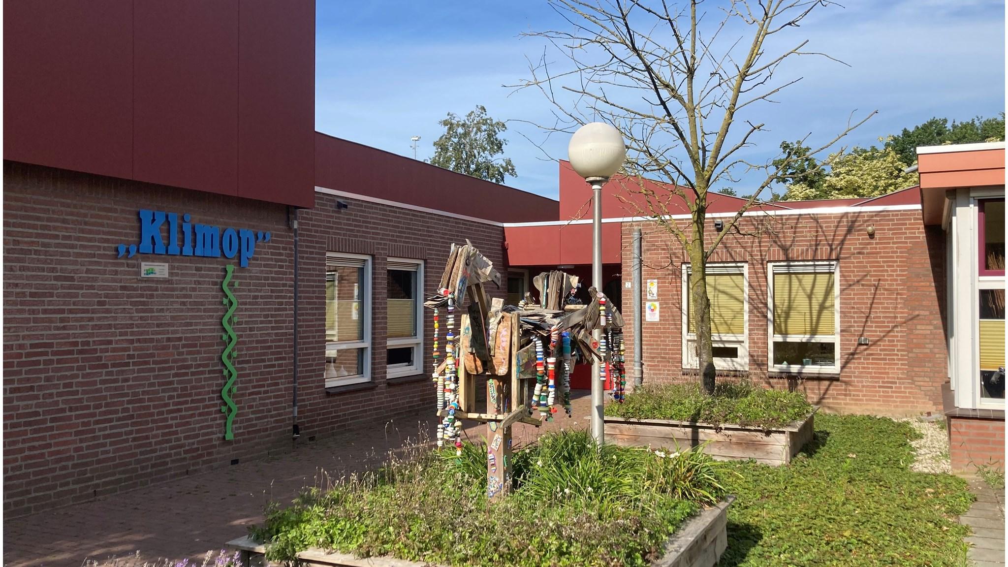 Foto van de ingang van Basisschool Klimop in Rijkevoort met versieringen en een kunstwerk op het schoolplein. Foto van de ingang van Basisschool Klimop in Rijkevoort met versieringen en een kunstwerk op het schoolplein.