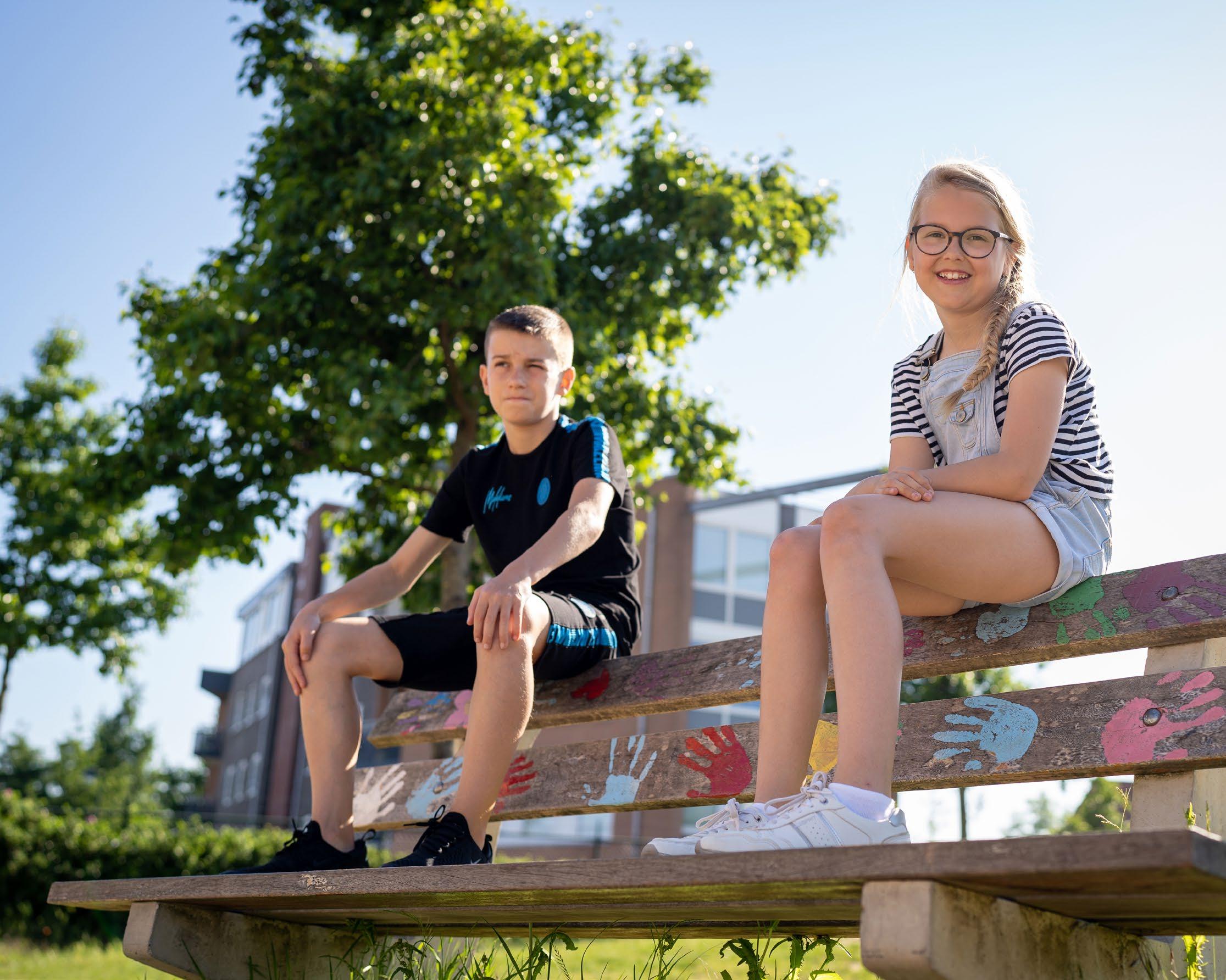 Foto van twee kinderen die ontspannen op een bankje zitten op het schoolplein van de Hubertusschool in Herten. Foto van twee kinderen die ontspannen op een bankje zitten op het schoolplein van de Hubertusschool in Herten.