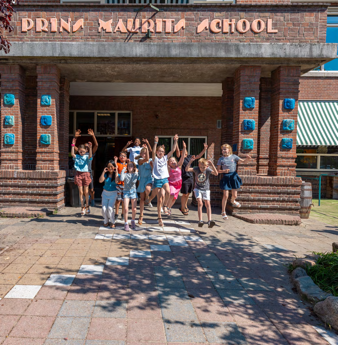 Groep blije kinderen springt voor de ingang van de Prins Mauritsschool in Delft. Groep blije kinderen springt voor de ingang van de Prins Mauritsschool in Delft.