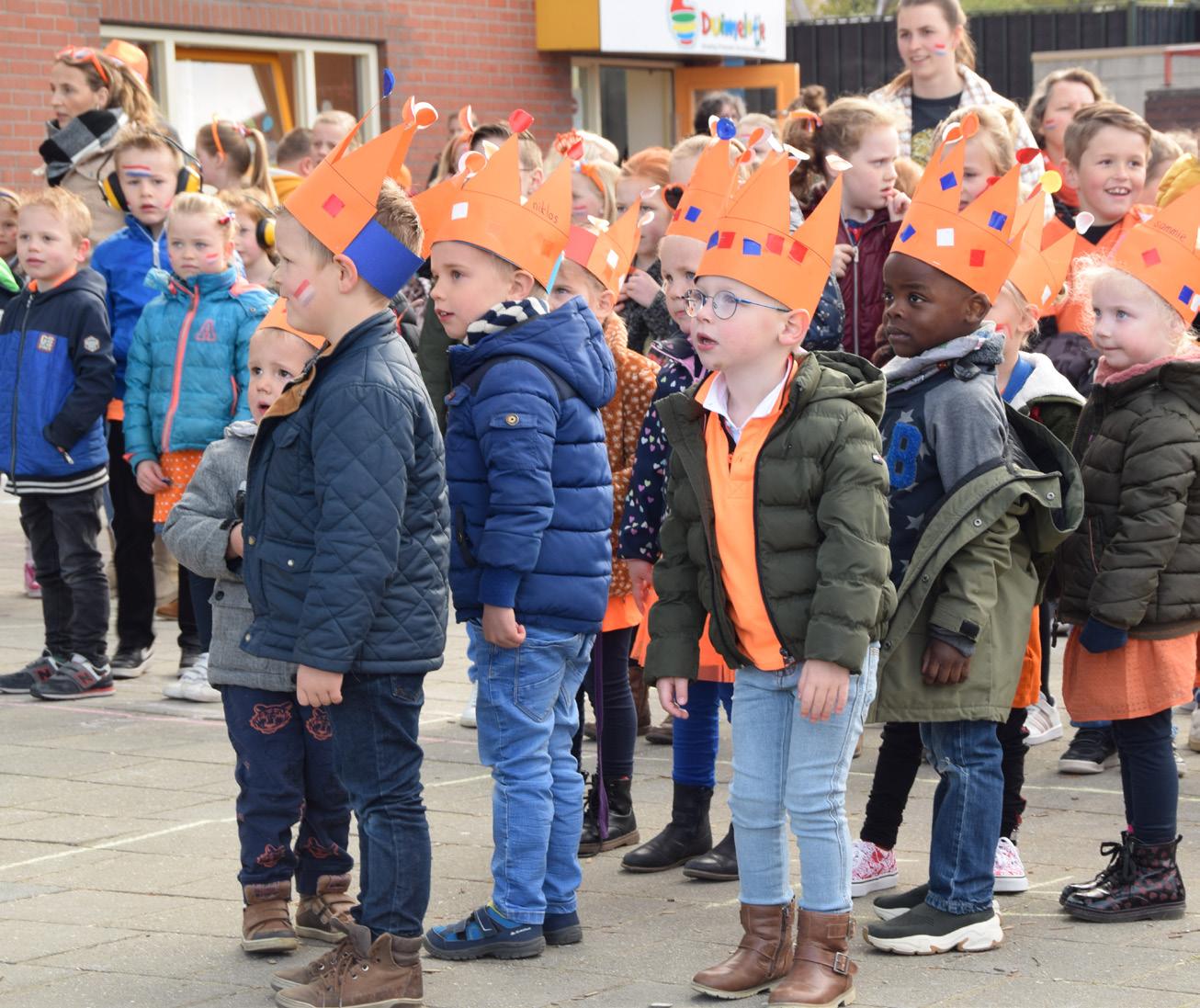 Groep kinderen met oranje kronen op het schoolplein van de Paasbergschool in Ede.