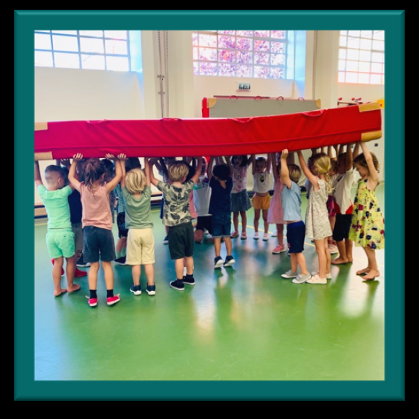 Groep kinderen van Basisschool de Odyssee in Utrecht tilt samen een grote rode mat op. Groep kinderen van Basisschool de Odyssee in Utrecht tilt samen een grote rode mat op.