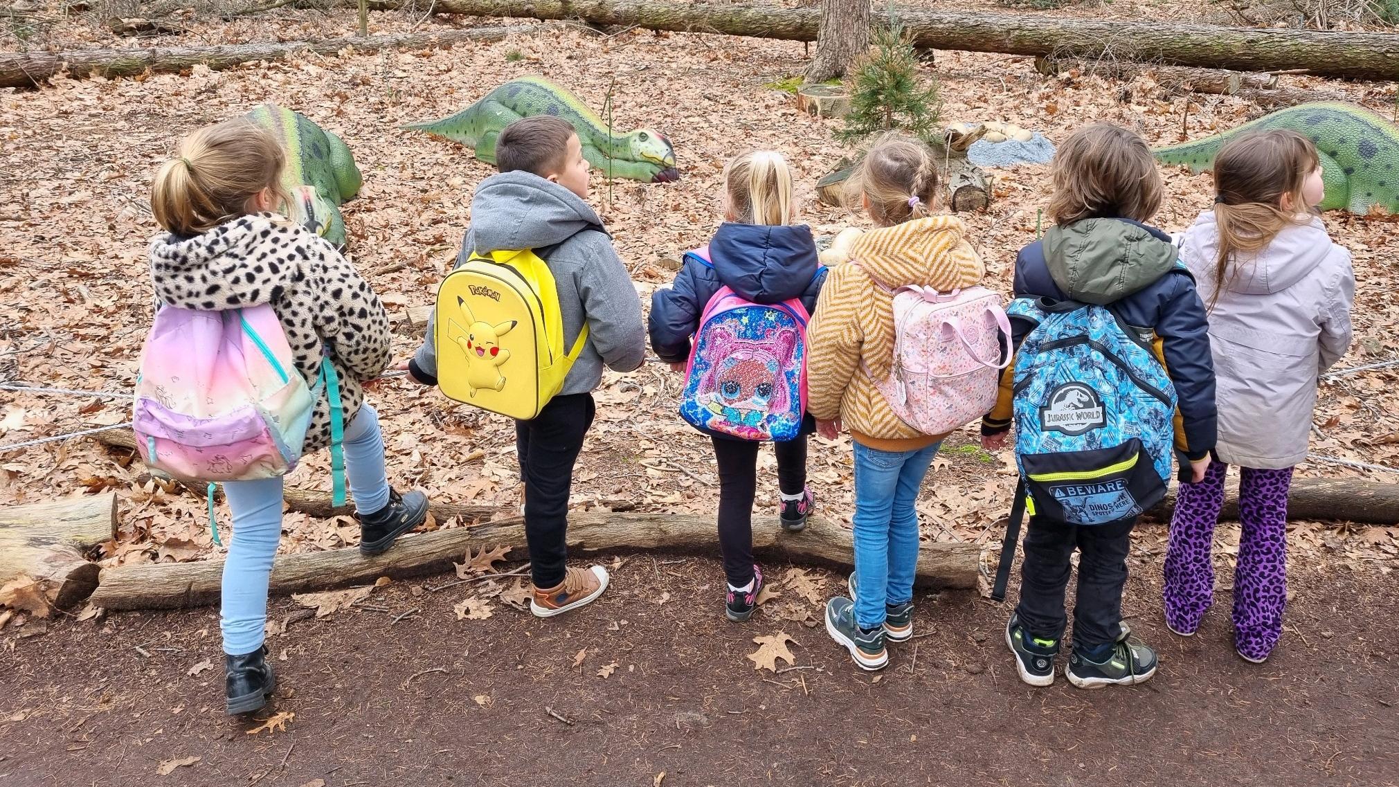 Groep kinderen van De Buizerd in Wijchen met rugzakken, kijkend naar dinosaurussen in het bos. Groep kinderen van De Buizerd in Wijchen met rugzakken, kijkend naar dinosaurussen in het bos.