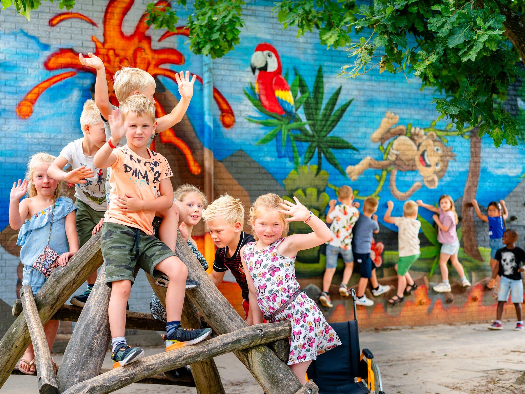 Groepsfoto van blije kinderen op het schoolplein van Kindcentrum De Morgenster in Zwolle, met een kleurrijke muurschildering op de achtergrond.