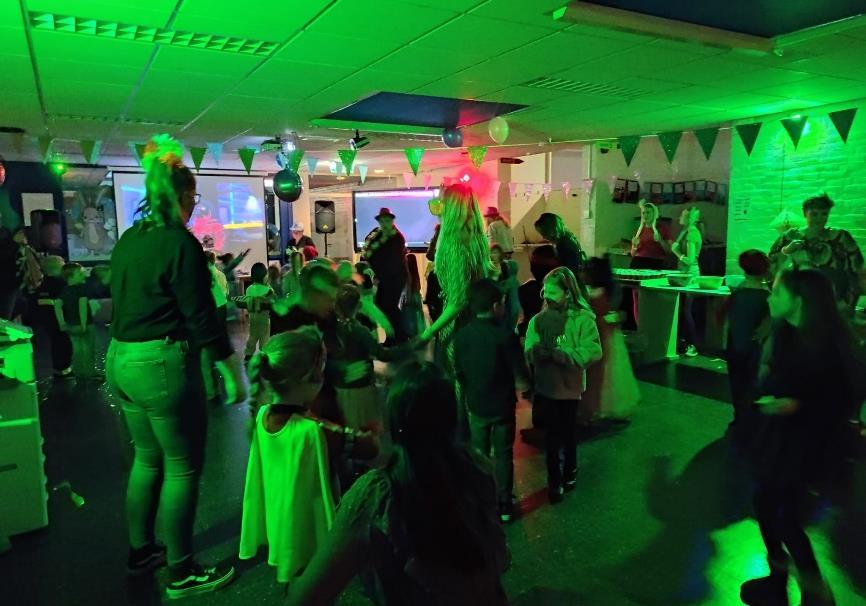 Het feest van CBS De Vossenburcht in Winschoten toont een levendige dansvloer met kinderen en volwassenen onder groen licht. Het feest van CBS De Vossenburcht in Winschoten toont een levendige dansvloer met kinderen en volwassenen onder groen licht.