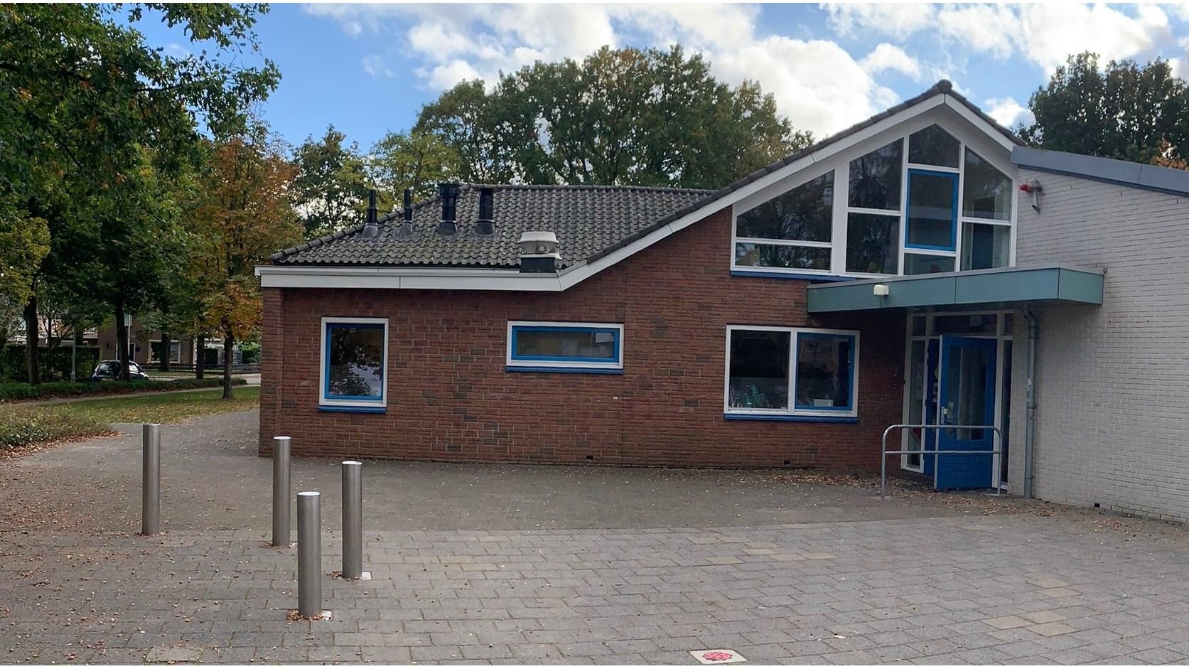 Het schoolgebouw van obs De Campherbeek in Zwolle, gelegen aan een ruimte met betonnen paden en groene bomen.