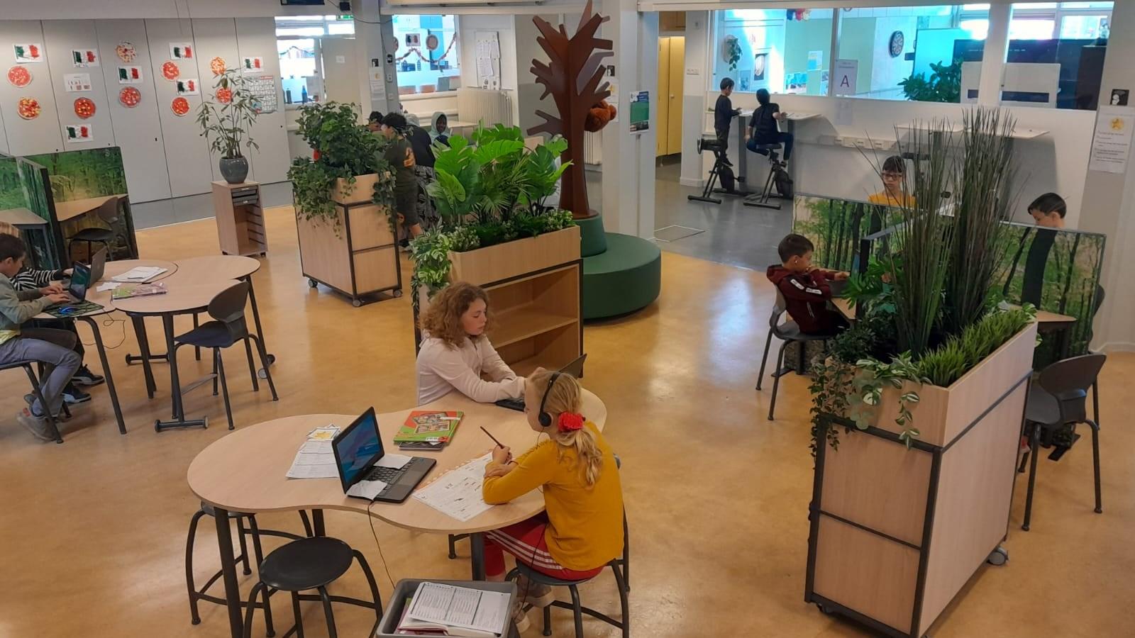 In de openruimte van Openbare Basisschool De Piramide in Edam werken leerlingen aan laptops tussen groene planten en natuurlijke elementen. In de openruimte van Openbare Basisschool De Piramide in Edam werken leerlingen aan laptops tussen groene planten en natuurlijke elementen.