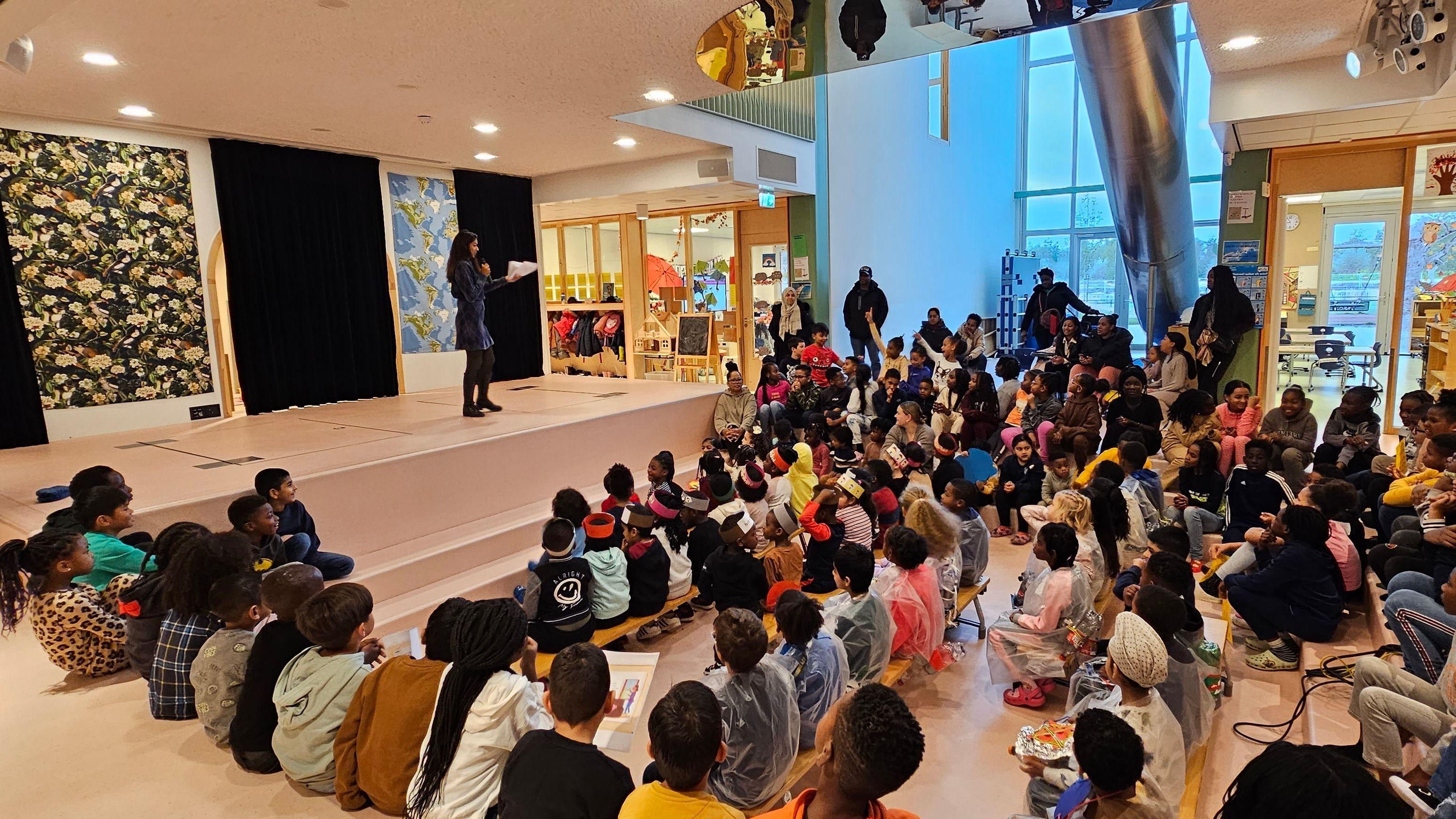 In het IKC Knotwilg in Amsterdam zitten kinderen aandachtig te luisteren naar een presentatie in de zaal. In het IKC Knotwilg in Amsterdam zitten kinderen aandachtig te luisteren naar een presentatie in de zaal.