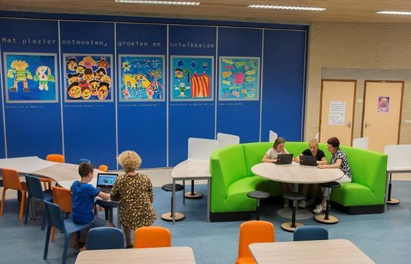 In het klaslokaal van Basisschool De Havenrakkers in Broek in Waterland werken leerlingen en docenten samen aan laptops, omringd door kleurrijke kunstwerken. In het klaslokaal van Basisschool De Havenrakkers in Broek in Waterland werken leerlingen en docenten samen aan laptops, omringd door kleurrijke kunstwerken.