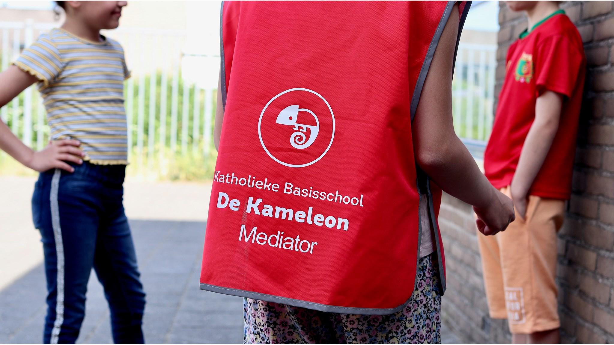 Katholieke Basisschool De Kameleon in Maarssen, met een leerling in een mediatorvest op het schoolplein. Katholieke Basisschool De Kameleon in Maarssen, met een leerling in een mediatorvest op het schoolplein.