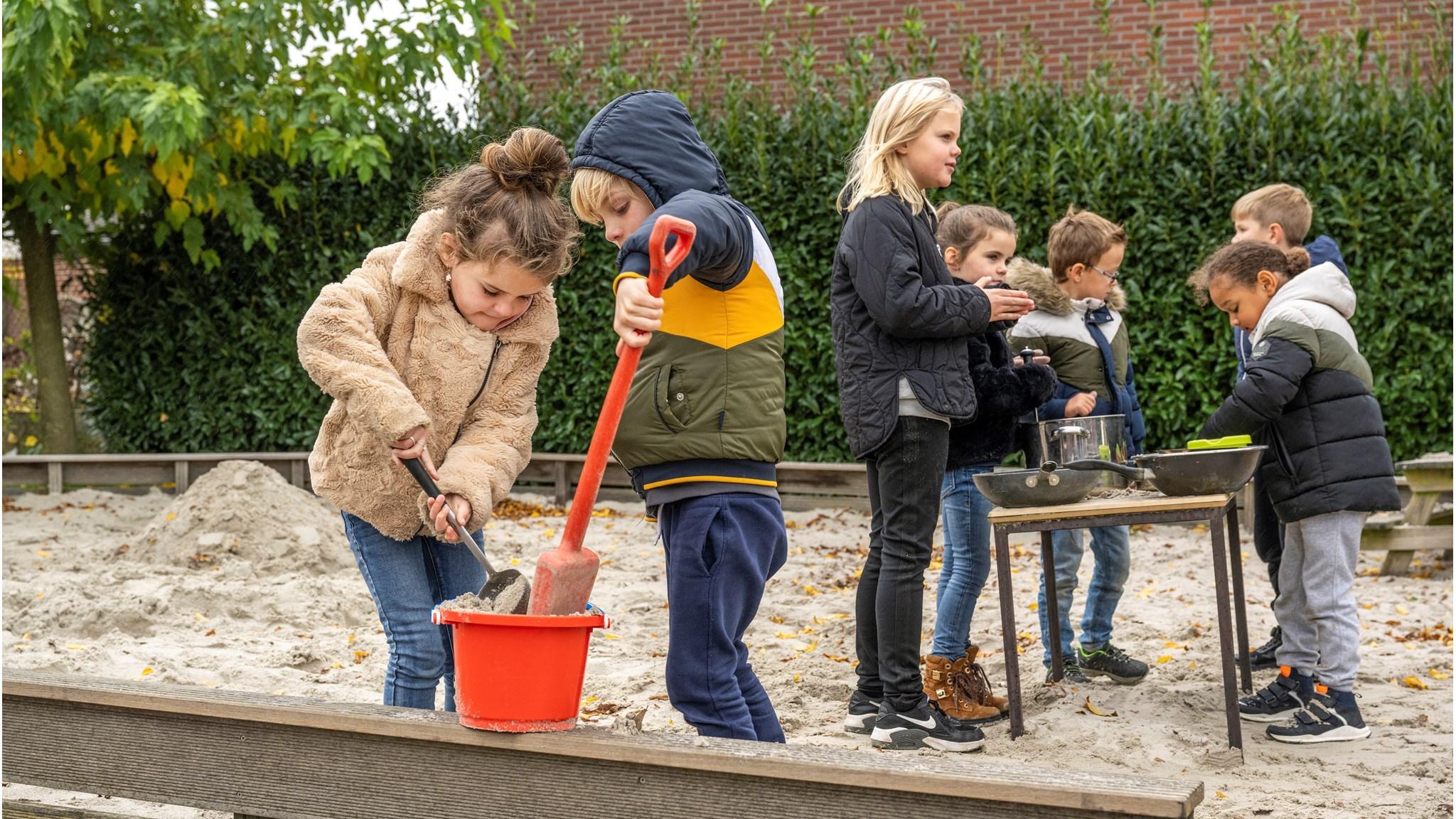 Kindcentrum Eikerwijs in Kessel: kinderen spelen en creëren in het schoolplein met zand en gereedschap.