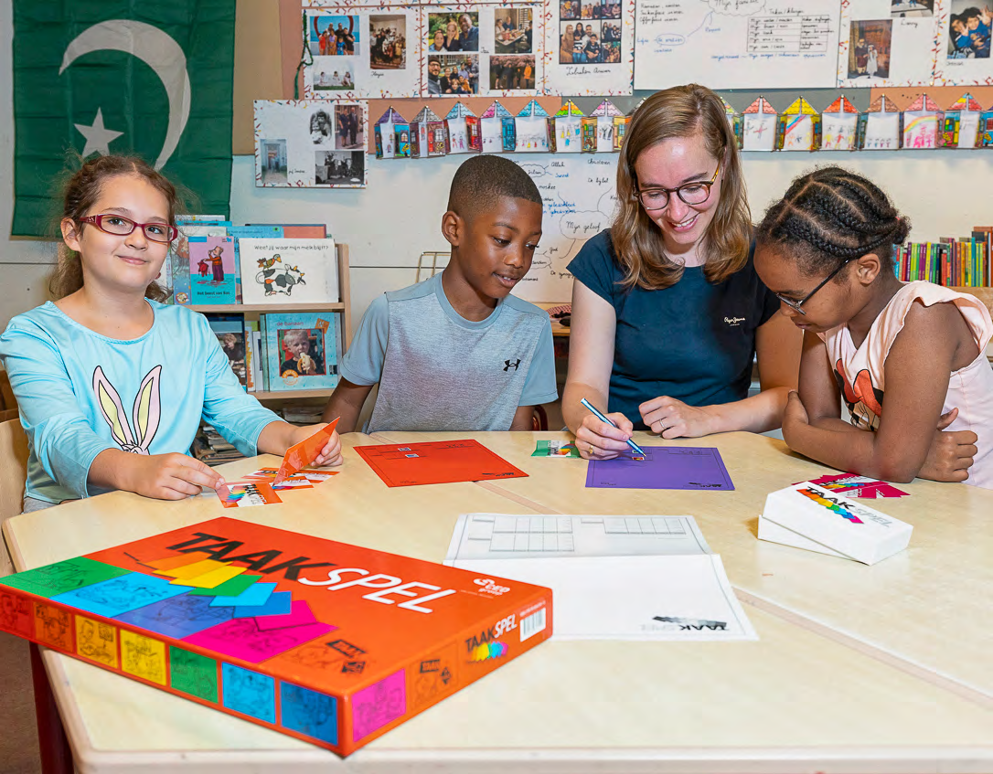 Kinderen en hun lerares zijn aan het knutselen met het 'TAAKSPEL' op CBS Mozaïek in Rotterdam.