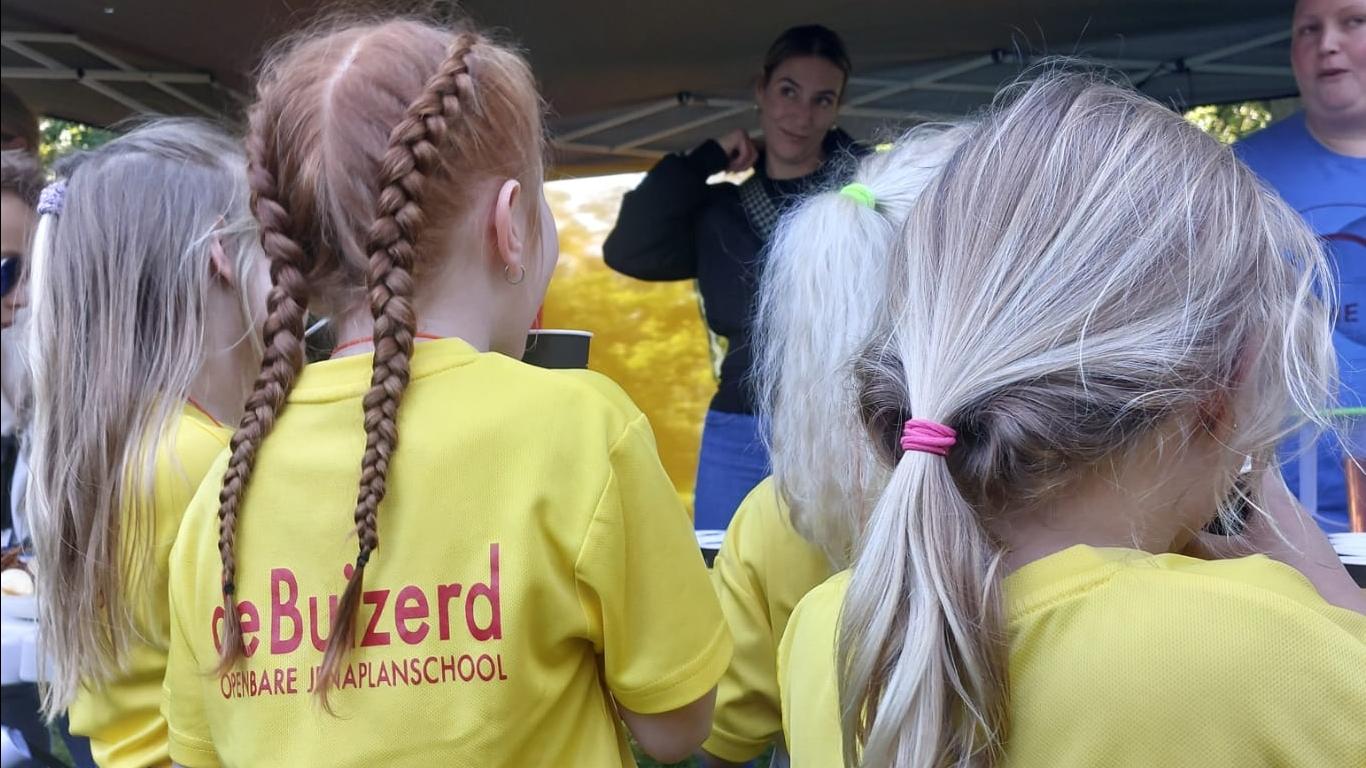 Kinderen in gele T-shirts van De Buizerd luisteren naar een activiteit op het schoolplein in Wijchen. Kinderen in gele T-shirts van De Buizerd luisteren naar een activiteit op het schoolplein in Wijchen.