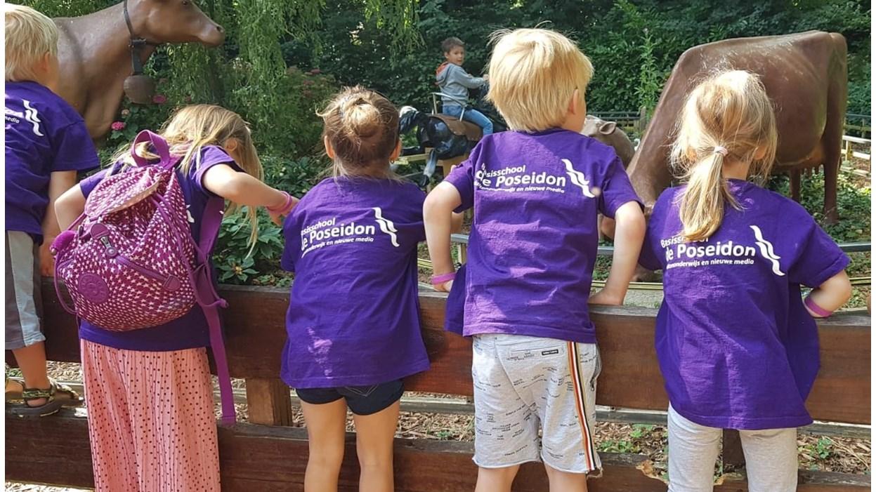 Kinderen met paarse shirts van basisschool De Poseidon kijken naar dieren in een schoolpleinactiviteit in Amsterdam.