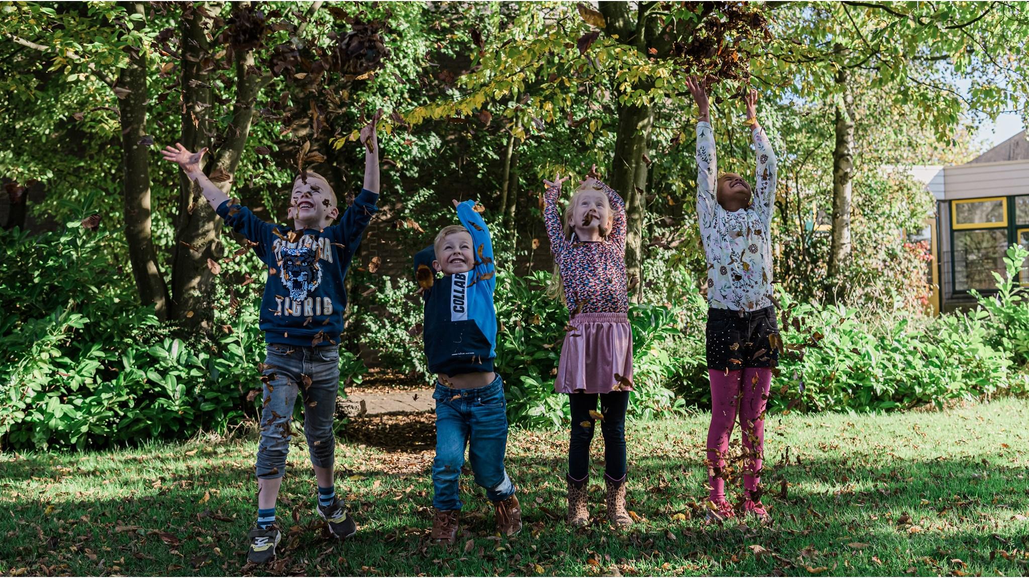 Kinderen spelen enthousiast met bladeren op het schoolplein van De Rietlanden in Marken.