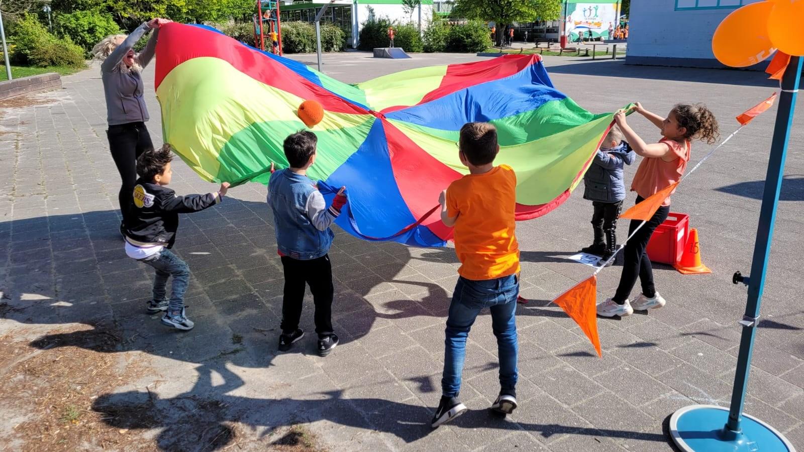 Kinderen spelen met een grote kleurenparachute op het schoolplein van De Twine in IJlst.
