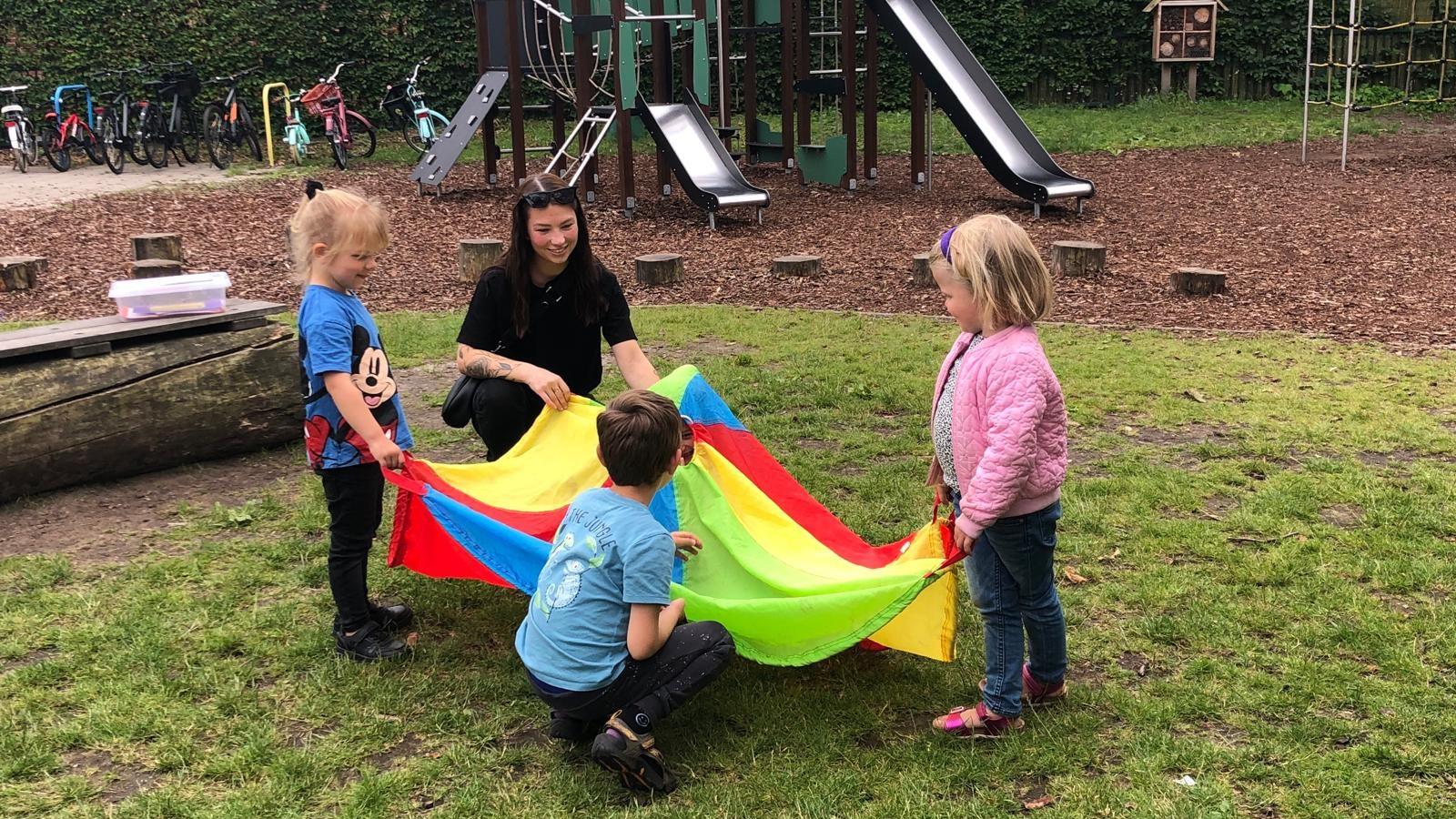 Kinderen spelen met een kleurrijke parachute onder begeleiding van een leerkracht op het schoolplein van Openbare Basisschool de Regenboog in Voorthuizen. Kinderen spelen met een kleurrijke parachute onder begeleiding van een leerkracht op het schoolplein van Openbare Basisschool de Regenboog in Voorthuizen.