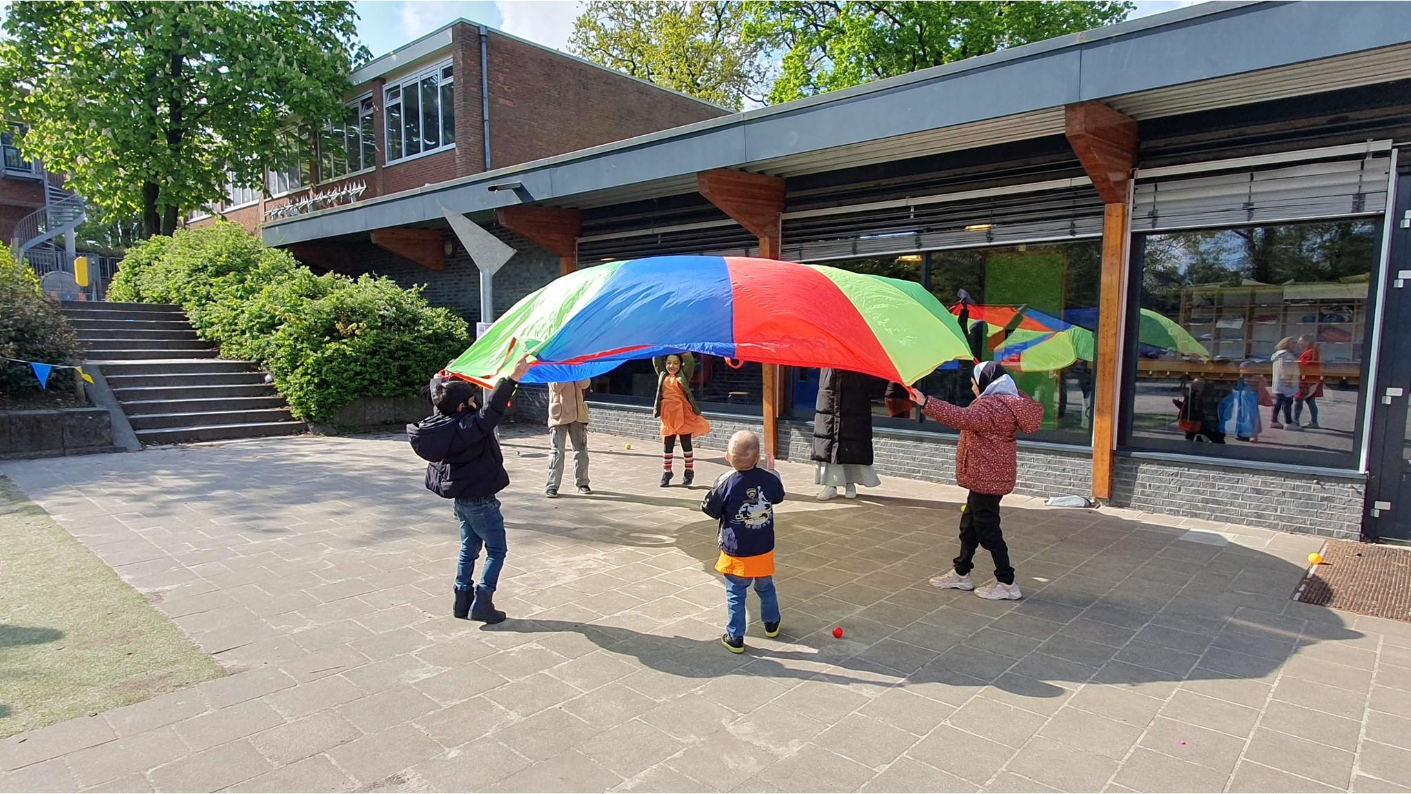 Kinderen spelen met een kleurrijke parachute op het schoolplein van Al Ummah in Enschede.