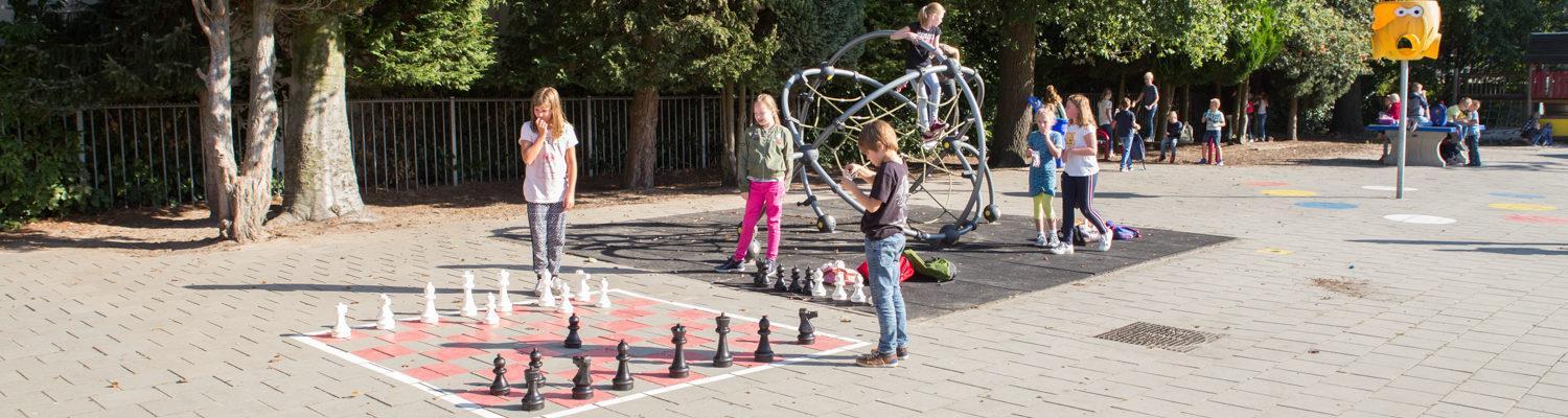 Kinderen spelen op het schoolplein van De Wegwijzer in Losser met een groot schaakbord en speeltoestellen. Kinderen spelen op het schoolplein van De Wegwijzer in Losser met een groot schaakbord en speeltoestellen.