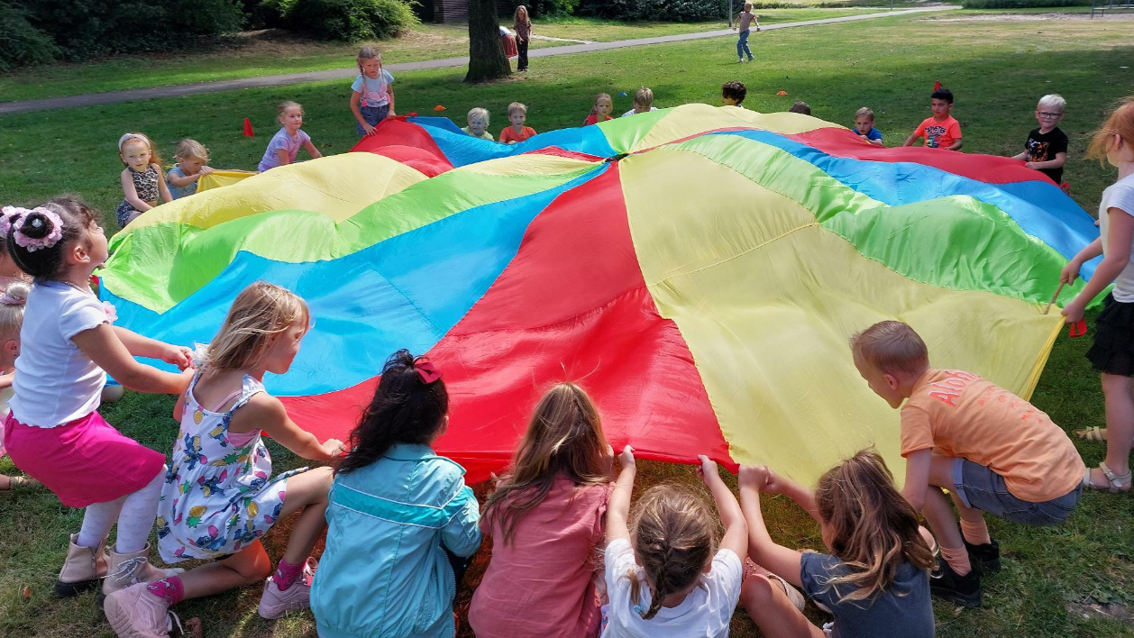 Kinderen spelen samen met een kleurrijke parachute op de speelplaats van Basisschool d'n Heiakker in Deurne. Kinderen spelen samen met een kleurrijke parachute op de speelplaats van Basisschool d'n Heiakker in Deurne.